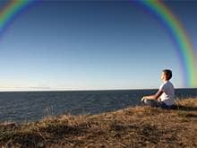 Meditating woman by canyon with a rainbow in the sky