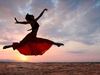 Woman dancing in desert against sunset