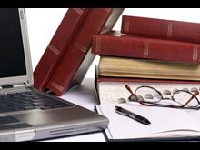 Laptop, eyeglasses, and books on a desk.