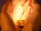 Two hands cupping lit lightbulb