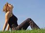 A woman sitting on a green grass field, looking up into a clear blue sky.
