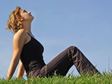 A woman sitting on a green grass field, looking up into a clear blue sky.