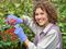 Smiling Red Curly-Haired Woman pruning flowers in green garden with gloves