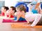 Three women practicing yoga in a gym with multi-colored yoga mats.