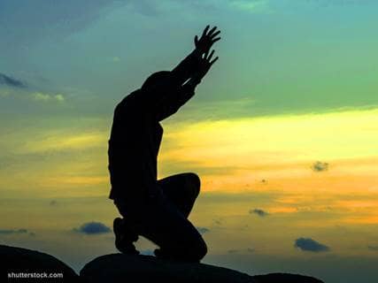 man praying arms up sunset